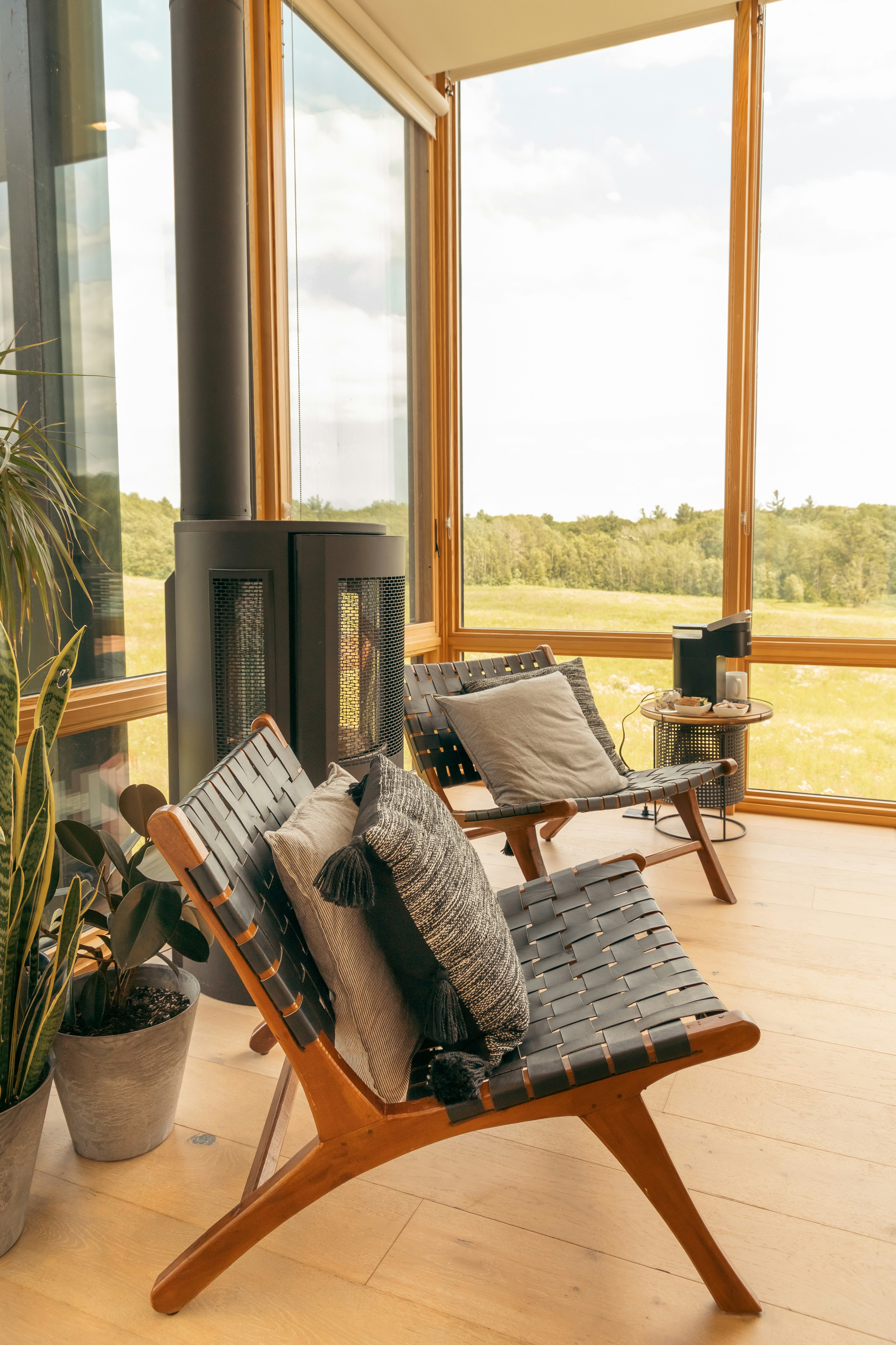 Considered Airbnb interior — woven chairs, woodburner, meadow view